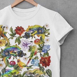 May include: White t-shirt with a colorful print of parrots, lizards, and flowers. The design features a variety of tropical plants and animals in a vibrant, whimsical style.