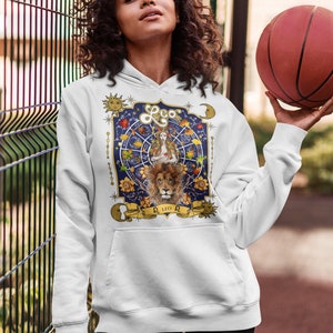May include: White hoodie with a graphic print of a lion and a woman with a crown, surrounded by stars and flowers. The text "Leo" is printed in gold on the graphic.