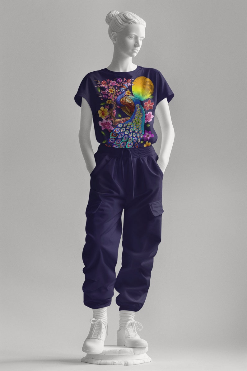May include: A navy blue t-shirt with a colorful peacock design and floral accents. The peacock is perched on a branch with a yellow moon in the background.