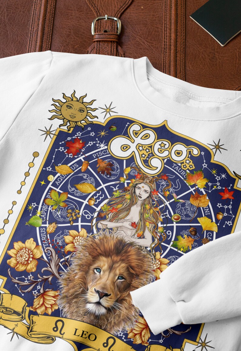 May include: White sweatshirt with a blue and gold zodiac design featuring the constellation Leo. The design includes a lion, a woman with long hair, and a circle with the zodiac signs. The text "Leo" is written in gold letters.