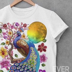 May include: White t-shirt with a colorful peacock design. The peacock is standing on a branch with pink flowers and a yellow moon in the background. The text "EVER POP studio" is printed on the bottom right corner of the shirt.