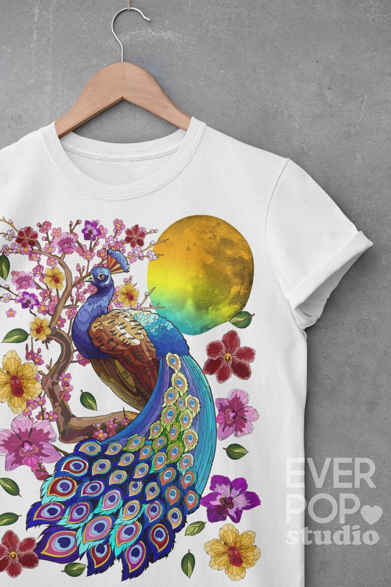 May include: White t-shirt with a colorful peacock design. The peacock is standing on a branch with pink flowers and a yellow moon in the background. The text "EVER POP studio" is printed on the bottom right corner of the shirt.