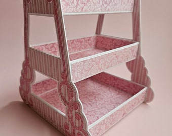 May include: A two-tiered pink and white shelf with a floral pattern. The shelf has a scalloped edge and is made of sturdy cardboard.