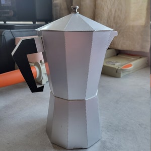 以下が含まれることがあります： 丸みを帯びたトップとハンドルが付いた銀色の金属製のコーヒーポット。ポットはテクスチャ加工された表面とわずかに丸みを帯びたベースを持っています。