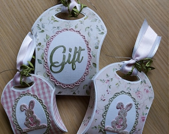 May include: Three small gift boxes with bunny and floral designs. The boxes are decorated with pink and green ribbon and have a cut-out handle. One box says "Gift" on the front.
