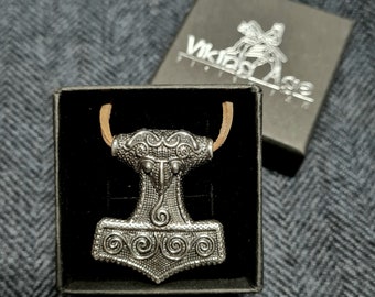 May include: A silver Mjolnir pendant with intricate details, in a black velvet box with a brown leather cord. The box has the text "Viking Age" printed on it.