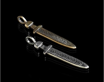 Könnte beinhalten: Zwei silberne und goldene Anhänger in Form von Schwertern mit einem strukturierten Design. Die Anhänger befinden sich auf einem schwarzen Hintergrund.