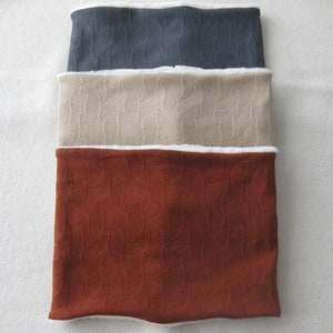 Könnte beinhalten: Drei Fleece-Halswärmer in verschiedenen Farben: Dunkelgrau, Beige und Rost. Jeder Halswärmer hat ein weißes Fleece-Futter.