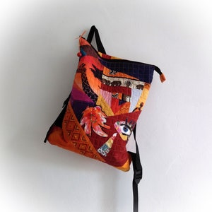 Puede incluir: Una mochila de patchwork colorida con un gran diseño de ojo y una correa negra. La mochila está hecha de diferentes telas y tiene una variedad de patrones, incluyendo formas geométricas, estampados de animales y diseños florales.
