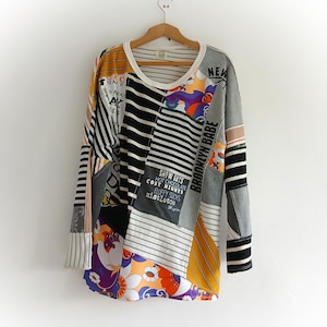 Puede incluir: Una camisa de manga larga con patchwork con cuello y puños blancos. La camisa presenta varios patrones, incluyendo rayas, diseños florales y texto que dice "Brooklyn Babe" y "Snow Days". La paleta de colores incluye negro, blanco, gris, amarillo y morado.