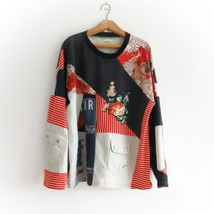 May include: A long-sleeve patchwork shirt featuring a mix of black, white, and red fabrics. The design includes striped patterns, a floral applique, and two front pockets with silver-toned buttons. Text on the shirt reads THE WAY I TOLD THE STORY.