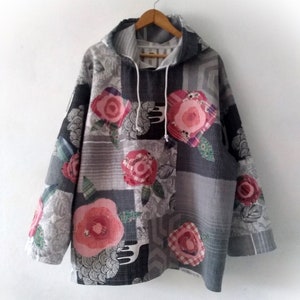 May include: A grey hooded sweatshirt with a patchwork design featuring pink and red floral patterns. The sweatshirt has a drawstring hood and a relaxed fit.