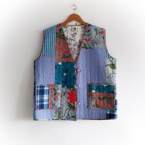Könnte beinhalten: Eine gesteppte Weste aus Patchwork-Stoff in Blautönen, Grün, Rot und Weiß. Die Weste hat einen Knopfverschluss und zwei Taschen.