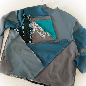 May include: A patchwork long-sleeve shirt in shades of teal, gray, and charcoal. The design features geometric shapes and a high neckline. Some patches have a printed design.