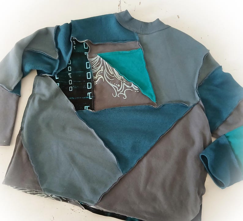 May include: A patchwork long-sleeve shirt in shades of teal, gray, and charcoal. The design features geometric shapes and a high neckline. Some patches have a printed design.