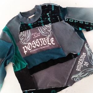 May include: A patchwork sweatshirt in shades of teal, gray, and black. The front features the word "POSSIBLE" in white script, with the phrases "Always Be Kind to Yourself" and "Eternity Forever." The sleeves and body are made of various fabric pieces.