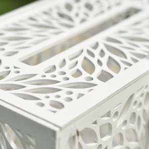 May include: A white wooden card box with intricate leaf-shaped cutouts. The box has a slot on top and a heart-shaped lock. The design is detailed and elegant, suitable for weddings or special events.
