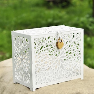 May include: A white wooden chest with intricate floral cutouts. The chest has a rectangular shape, a hinged lid, and a heart-shaped lock. The design is delicate and decorative, suitable for storage or display.