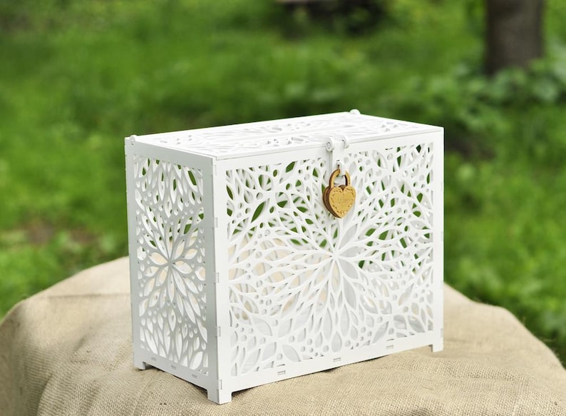 May include: A white wooden chest with intricate floral cutouts. The chest has a rectangular shape, a hinged lid, and a heart-shaped lock. The design is delicate and decorative, suitable for storage or display.