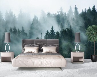 May include: A bedroom featuring a wall mural of a dense, misty forest with tall evergreen trees. The bed has a gray upholstered headboard and light-colored bedding. Two matching bedside tables with gray lamps flank the bed, and a potted tree stands to the right.