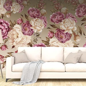 May include: A white sofa with three cushions and a light gray throw blanket, positioned in front of a wall covered in floral wallpaper featuring large cream and deep magenta peonies with brown foliage on a light tan background, next to a floor lamp.