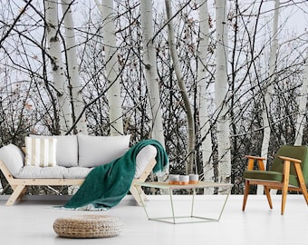 May include: A light gray sofa with a striped pillow and a dark green throw blanket, a wooden coffee table with three small bowls, a green armchair with wooden legs, and a round woven ottoman against a wall mural of white birch trees.