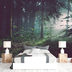 Puede incluir: Un dormitorio con una cama de ropa blanca y un camino de mesa gris, flanqueada por dos mesitas de noche cúbicas de madera con lámparas blancas. La pared detrás de la cama muestra un mural de un bosque denso y brumoso con árboles altos.