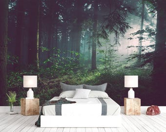 May include: A bedroom featuring a bed with white bedding and a gray runner, flanked by two wooden cube nightstands topped with white lamps. The wall behind the bed displays a large-scale mural of a dense, misty forest with tall trees.