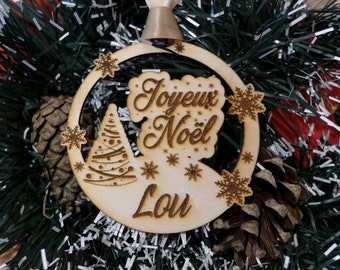 Peut inclure: Ornement de Noël en bois avec l'inscription "Joyeux Noël Lou" gravée. L'ornement présente des motifs de sapin de Noël et de flocons de neige. Il est suspendu à un sapin de Noël avec des pommes de pin et des guirlandes.