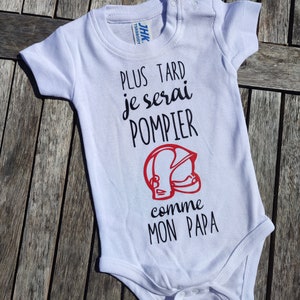 Peut inclure: Body bébé blanc avec l'inscription "PLUS TARD je serai POMPIER comme MON PAPA" en noir et un casque de pompier rouge. Le body a des manches courtes et des boutons-pression.
