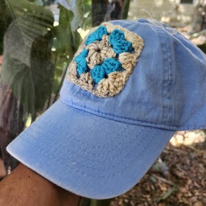 May include: A light blue baseball cap with a crocheted square patch in shades of blue and beige.