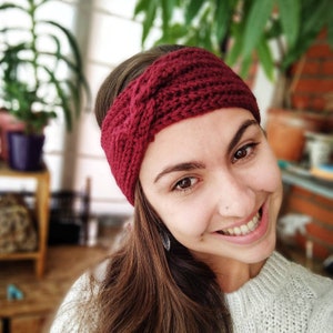 May include: A close-up of a woman wearing a burgundy crocheted headband. The headband is knotted on top of her head and has a simple, textured design.