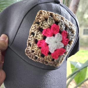 May include: A gray baseball cap with a brown, white, and pink crocheted square patch on the front.
