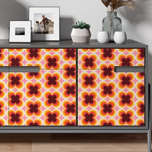 May include: A grey dresser with three drawers, each featuring a retro-style pattern of orange, pink and brown circles. The dresser has a simple design with black handles and sits on a light wood floor.