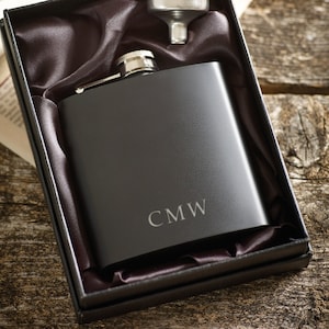 May include: A black hip flask with a silver top and a funnel in a black velvet box. The flask is engraved with the initials "CMW".