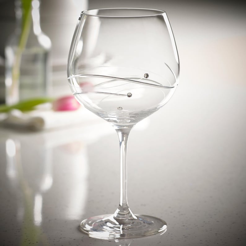 May include: A clear glass wine glass with a swirl design and small crystal accents. The glass has a wide bowl and a long stem.