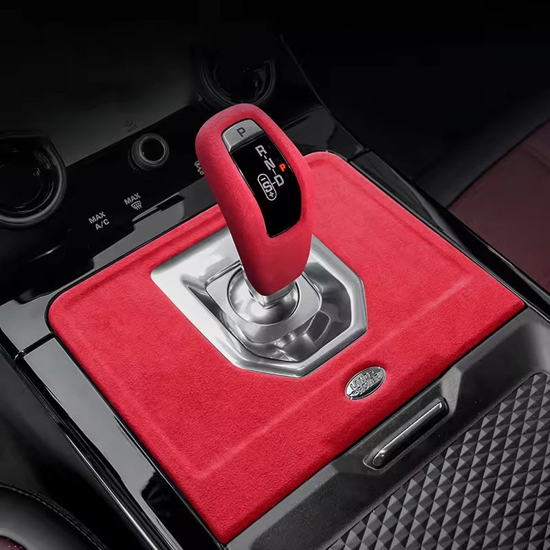 May include: Red leather gear shift knob with a silver base and a black plastic gear selector with the letters "P, R, N, D" and a red "P" on a black car interior with a red leather console.