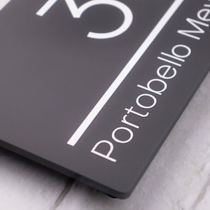 May include: A gray rectangular sign with white lettering. The number "25" is at the top of the sign, and the word "Portobello" is below it.