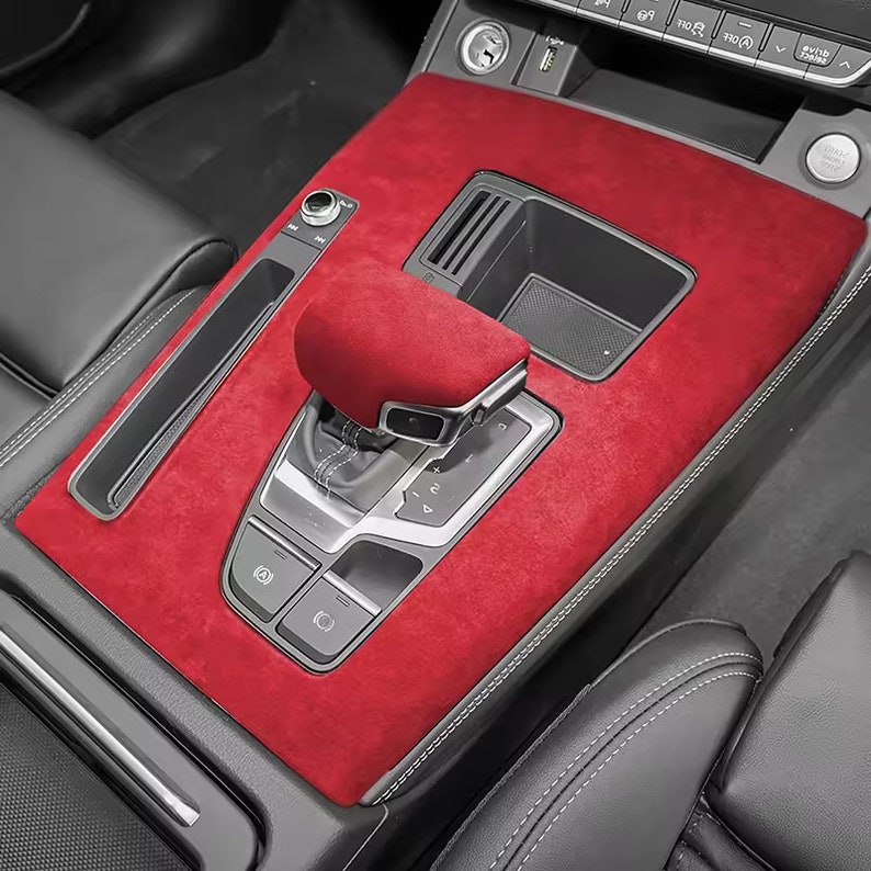May include: Red suede car interior trim kit with a gear shifter and buttons. The trim kit is designed to fit the center console of a car.