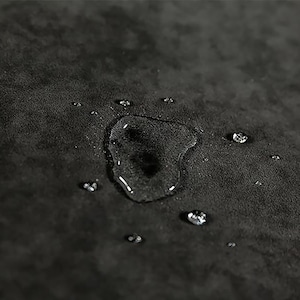 May include: Close-up of a dark gray fabric surface with water droplets on it. The fabric has a textured appearance, and the water droplets are round and clear.