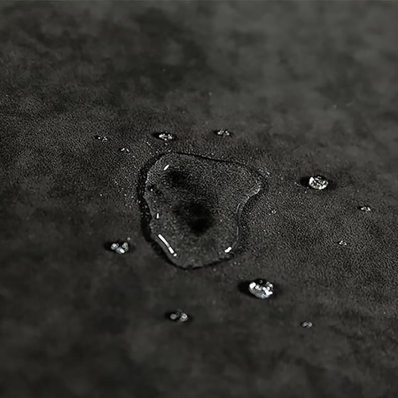 May include: Close-up of a dark gray fabric surface with water droplets on it. The fabric has a textured appearance, and the water droplets are round and clear.