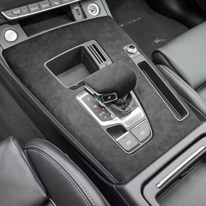 May include: Close-up of a black leather car interior with a gear shifter and a black suede centre console. The gear shifter has a black leather gaiter and a silver gear selector with the letters "R", "N", "P", "D", and "S".
