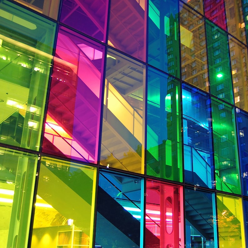 Pode incluir: Um detalhe arquitet&ocirc;nico vibrante com uma grade de pain&eacute;is de vidro coloridos. Os pain&eacute;is exibem um espectro de tons, incluindo verde, amarelo, rosa e azul, refletindo as estruturas circundantes e o c&eacute;u. O design cria uma composi&ccedil;&atilde;o din&acirc;mica e visualmente envolvente.
