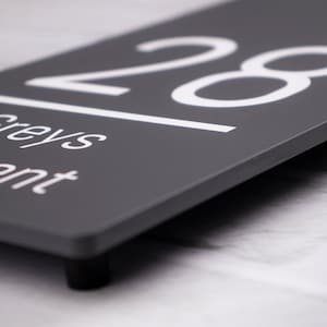 May include: A gray house number sign with white lettering. The number 28 is displayed on the sign, along with the words "Greys" and "ent".
