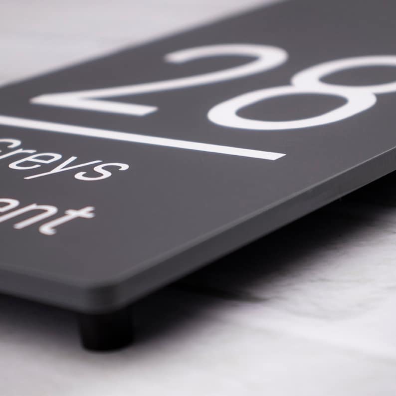 May include: A gray house number sign with white lettering. The number 28 is displayed on the sign, along with the words "Greys" and "ent".