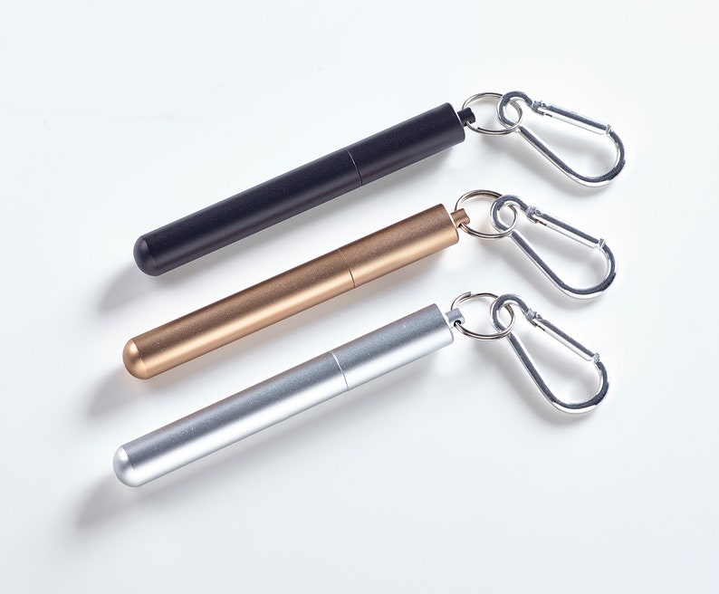 May include: Three metal straws with attached carabiners. The straws are black, gold, and silver.