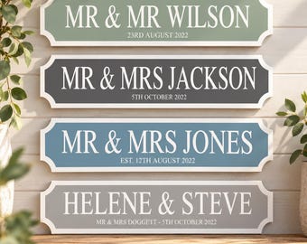 May include: Four rectangular wall signs with decorative notched ends. The signs feature white text on sage green, dark gray, blue, and light gray backgrounds, displaying names like MR & MR WILSON, MR & MRS JACKSON, MR & MRS JONES, and HELENE & STEVE.