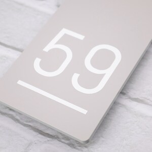 May include: A light gray rectangular sign with the number 59 printed in white.