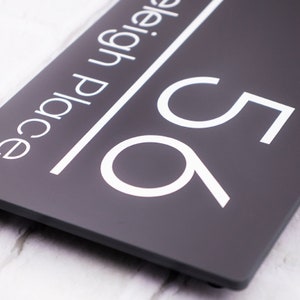 May include: A dark gray house number sign with white lettering. The number 95 is displayed in a modern font. The text "Leigh Place" is also displayed in white.