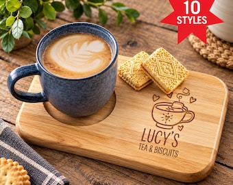May include: A rectangular bamboo serving tray with a circular indentation for a blue ceramic mug filled with latte art. The tray features an engraved illustration of a teacup and the text "Lucy's Tea & Biscuits" alongside two square biscuits.